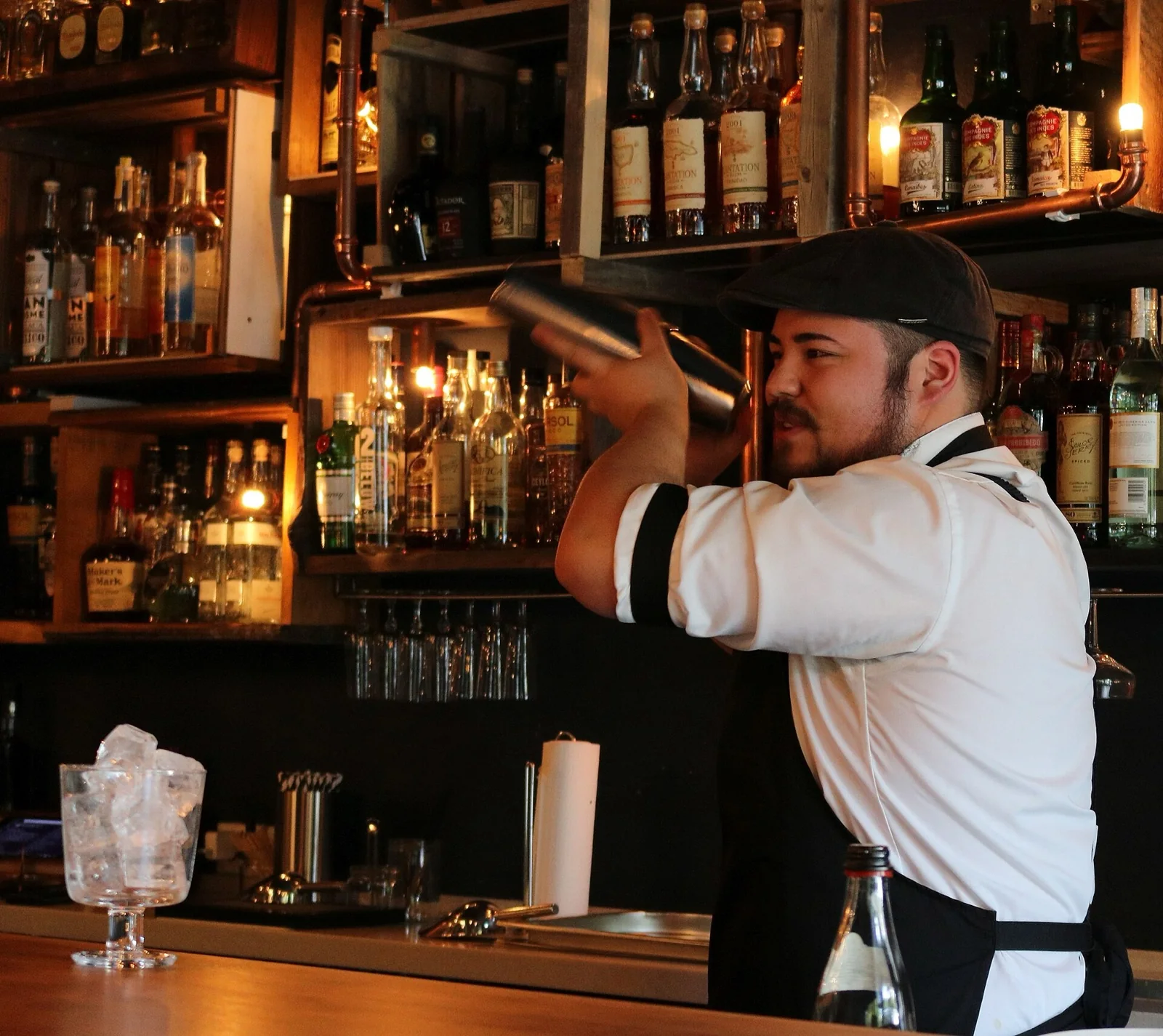 Bartender shaking a cocktail behind a bar with bottles on the back shelf